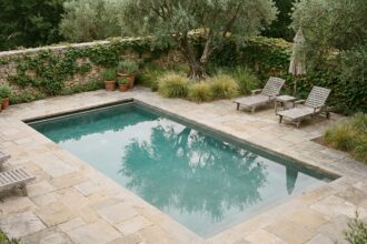 Piscine en béton aménagée dans un jardin paysager avec dallage en pierre naturelle et transats en teck